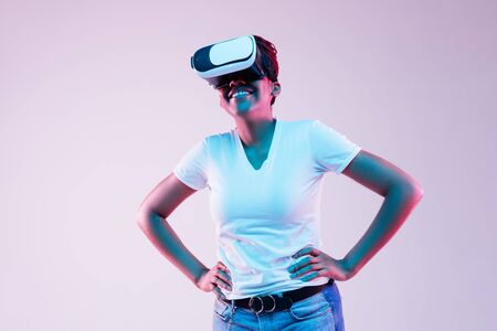 Portrait of young african-american womans playing in VR-glasses in neon light on gradient...