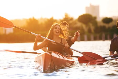 Confident young caucasian couple kayaking on river together with sunset in the backgrounds. Having fun in leisure activity. Romantic and happy woman and man on the kayak. Sport, relations concept.の写真素材