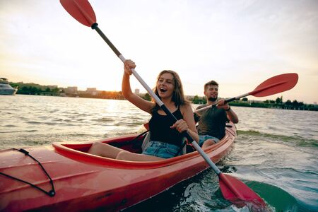 Confident young caucasian couple kayaking on river together with sunset in the backgrounds. Having...