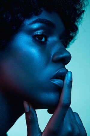 Marvelous night. Portrait of female fashion model in neon light on gradient background. Beautiful african woman with trendy make-up and well-kept skin. Vivid style, beauty, cosmetics concept.の写真素材