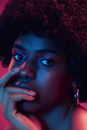 Summers sunset. Portrait of female fashion model in neon light on gradient background. Beautiful african woman with trendy make-up and well-kept skin. Vivid style, beauty, cosmetics concept.の写真素材