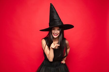 Young brunette woman in black hat and costume on red background. Attractive caucasian female model....