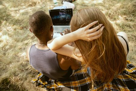 Young multiethnic international romantic couple outdoors at the meadow in sunny summer day. African-american man and caucasian woman watching cinema together. Concept of relationship, summertime.の写真素材