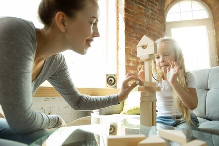 Learn to make a decision. Teacher and little girl, or mom and daughter. Homeschooling. Sitting on the sofa and working with wooden constructor, having fun. Education, school, studying concept.の写真素材