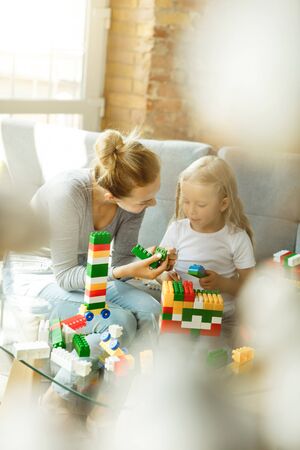 Female caucasian teacher and little girl, or mom and daughter. Homeschooling. Sitting on the sofa with plastic constructor, learning, talking and having fun. Education, school, studying concept.の写真素材