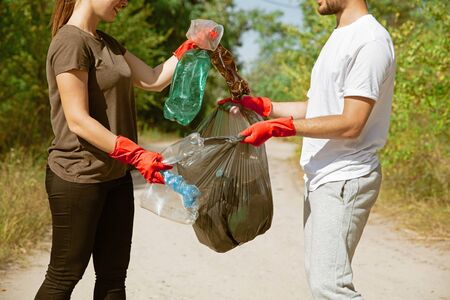 Enjoy what youre doing. Group of volunteers tidying up rubbish on beach in sunny day. Young man and woman take care of nature and environment, taking bottles and packs away. Concept of ecology.の写真素材