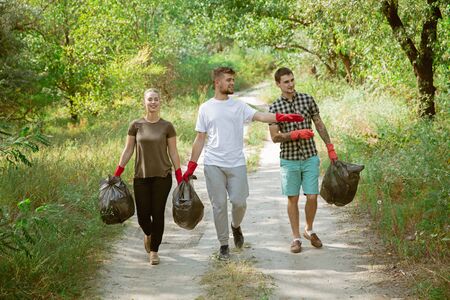 Build healthy home together. Group of volunteers tidying up rubbish on beach in sunny day. Young men...