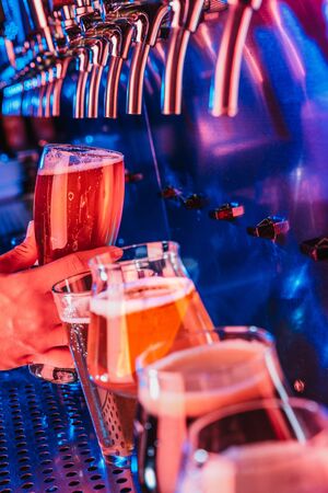 Hand of bartender pouring a large lager beer in tap. Bright and modern neon light, males hands. Pouring beer for client. Side view of young bartender pouring beer while standing at the bar counter.の写真素材
