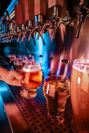 Hand of bartender pouring a large lager beer in tap. Bright and modern neon light, males hands....