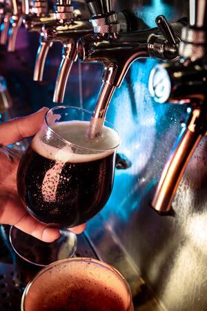 Hand of bartender pouring a large ale, porter, stout beer in tap. Bright and modern neon light,...