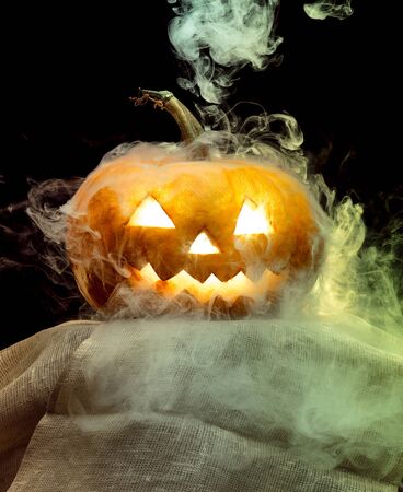 Halloween pumpkin head jack-o-lantern with scary evil face. Seasonal illuminated decoration. Looks scary, neon light, white smoke and dark background. Holidays. Black friday, sales. Night of fear.の写真素材
