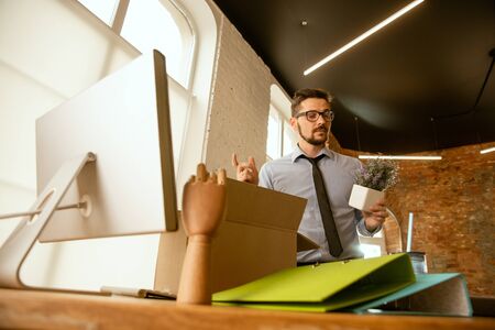 Beginning. A young businessman moving in the office, getting new work place. Young male office worker equips new cabinet after promotion. Looks happy. Business, lifestyle, new life concept. Unpacking.の写真素材
