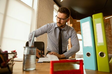 In process. A young businessman moving in the office, getting new work place. Young male office worker equips new cabinet after promotion. Looks happy. Business, lifestyle, new life concept. Unpacking.の写真素材