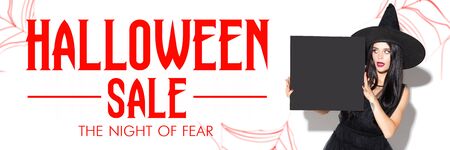 Young brunette woman in black hat on scary white background. Attractive caucasian female model smiling. Halloween sales, black friday, cyber monday, autumn concept. Flyer for ad. Holding copyspace.の写真素材