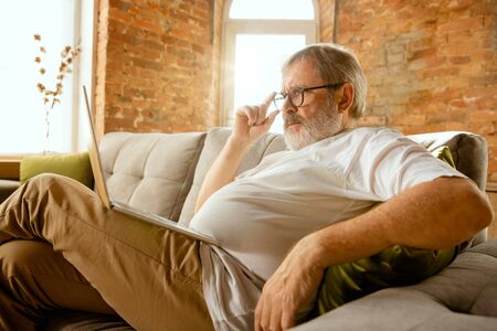 Senior man working with laptop at home - concept of home studying. Caucasian male model sitting on...