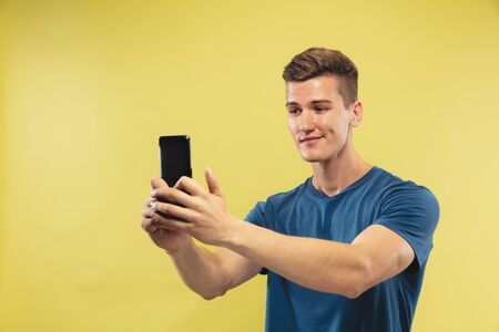 Caucasian young mans half-length portrait on yellow studio background. Beautiful male model in blue...