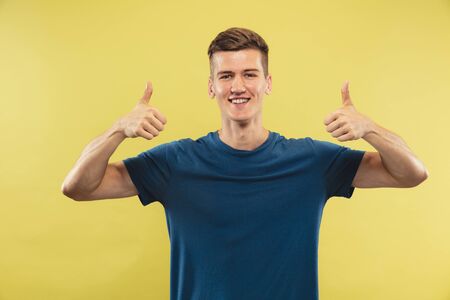 Caucasian young mans half-length portrait on yellow studio background. Beautiful male model in blue...