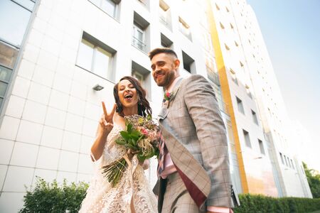 Caucasian romantic young couple celebrating marriage in city. Tender bride and groom on modern citys street. Family, relation, love concept. Contemporary wedding. Crazy happy, playful like child.の写真素材