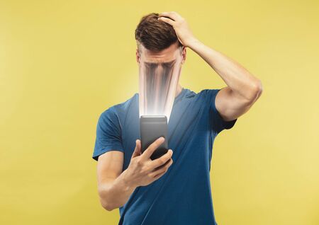 Young man using smartphone isolated on yellow studio background. Concept of human emotions, facial...
