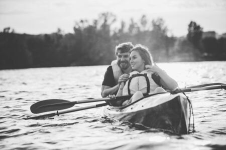 Happy young caucasian couple kayaking on river with sunset in the backgrounds. Having fun in leisure...