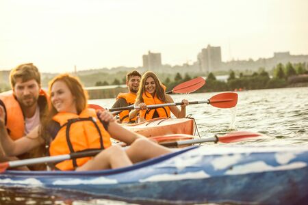 Happy young caucasian group of friends kayaking on river with sunset in the backgrounds. Having fun...