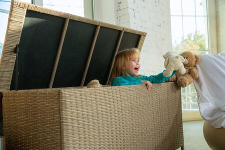 Little girls in soft warm pajamas playing at home. Caucasian children in colorful clothes having fun together. Childhood, home comfort, happiness. Sitting in a large wicker box and laughting.の写真素材