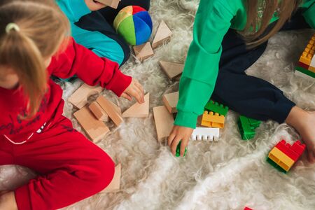 Little girls in soft warm pajamas playing at home. Caucasian children in colorful clothes having fun together. Childhood, home comfort, happiness. Sitting on the floor and making constructor.の写真素材