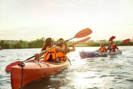Happy young caucasian group of friends kayaking on river with sunset in the backgrounds. Having fun...
