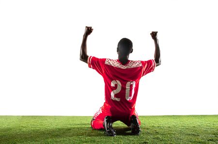 Professional african-american football or soccer player of red team in motion isolated on white studio background. Fit man in action, excitement, emotional moment. Concept of movement at gameplay.の写真素材