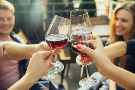 People clinking glasses with wine on the summer terrace of cafe or restaurant. Happy cheerful friends celebrate summer or autumn fest. Close up shot of human hands, lifestyle.の写真素材