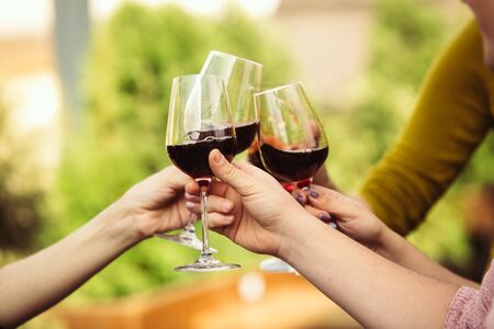 People clinking glasses with wine on the summer terrace of cafe or restaurant. Happy cheerful friends celebrate summer or autumn fest. Close up shot of human hands, lifestyle.の写真素材