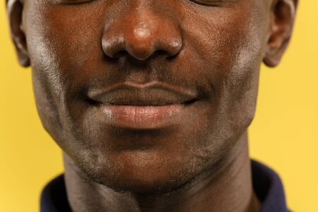 African-american young man's close up portrait on yellow studio background. Beautiful male model with well-kept skin. Concept of human emotions, facial expression, sales, ad. Looks calm and smiling.の写真素材