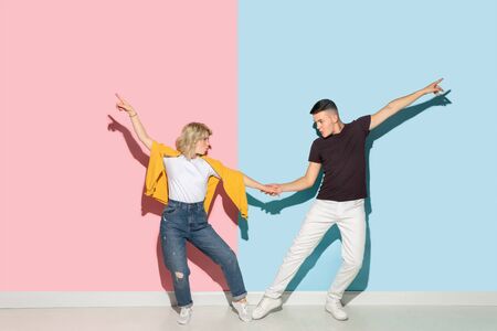 Young emotional man and woman in bright casual clothes posing on pink and blue background. Concept of human emotions, facial expession, relations, ad. Beautiful caucasian couple dancing together.の写真素材