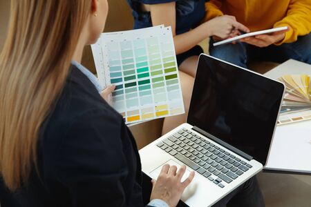 Interior designer working with young couple. Lovely family and professional designer or architector discussing conept of future interior, working with colour palette, room drawings in modern office.の写真素材