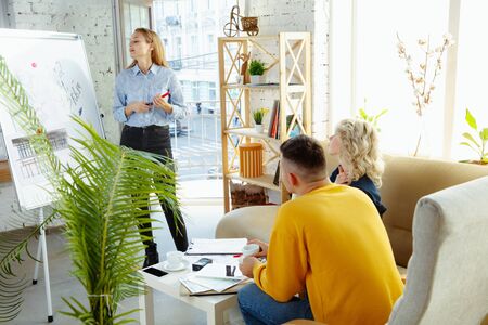 Interior designer working with young couple. Lovely family and professional designer or architector discussing conept of future interior, working with colour palette, room drawings in modern office.の写真素材