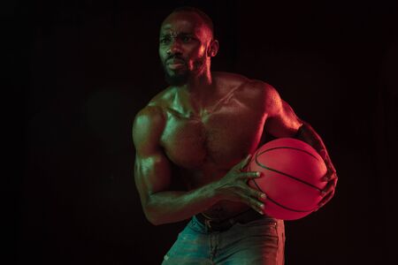 African-american muscular young basketball player in action of gameplay training, practicing in neon...