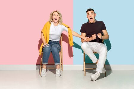 Young emotional man and woman in bright casual clothes posing on pink and blue background. Concept...
