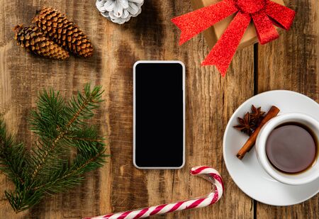 Mock up blank empty screen of smartphone on the wooden  with colorful holidays decoration, tea and gifts.の写真素材
