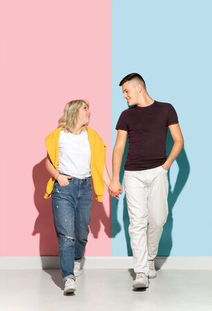 Young emotional man and woman in bright casual clothes posing on pink and blue background. Concept of human emotions, facial expession, relations, ad. Beautiful caucasian couple walking holding hands.の写真素材