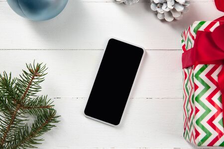 Mock up blank empty screen of smartphone on the white wooden background with colorful holiday's decoration and gifts. Copyspace, negative space for your advertising. 31 of December, New Year concept.の写真素材