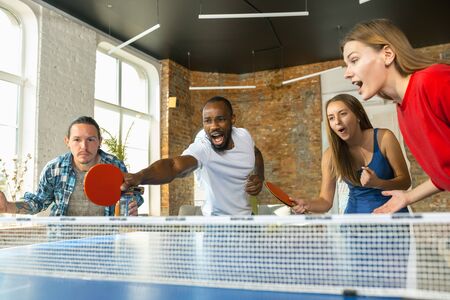 Young people playing table tennis in workplace, having fun.