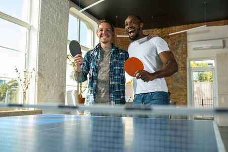 Young people playing table tennis in workplace, having fun.