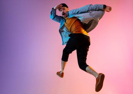Full length portrait of happy jumping man wearing casual clothes in neon light isolated on gradient background. Emotions, ad concept. Expressive hurrying up, late for work or sale, shopping.の写真素材