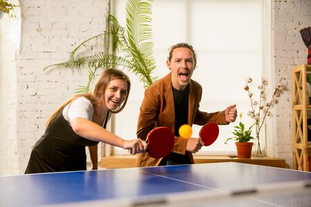 Young people playing table tennis in workplace, having fun. Friends in casual clothes play table tennis together at sunny day. Concept of leisure activity, sport, friendship, team-building, teamwork.の写真素材