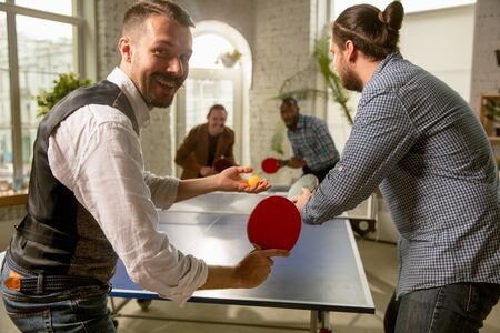 Young people playing table tennis in workplace, having fun. Friends in casual clothes play table...