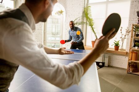 Young men playing table tennis in workplace, having fun. Friends in casual clothes play table tennis...