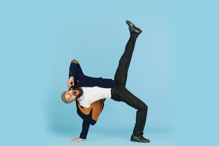 Young caucasian businessman having fun dancing break dance on blue studio background. Management, flexible, freedom, professional occupation, alternative way of modern working. Loves his job. Copyspace.の写真素材