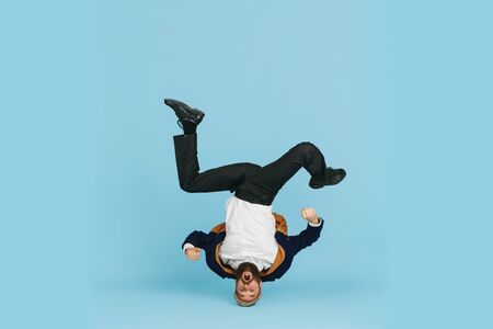 Young caucasian businessman having fun dancing break dance on blue studio background. Management,...