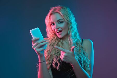 Caucasian young womans portrait on gradient background in neon light. Beautiful female model with unusual look. Concept of human emotions, facial expression, sales, ad. Making selfie, bet, purchases.の写真素材