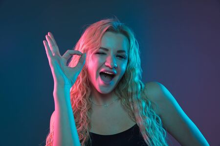 Caucasian young womans portrait on gradient background in neon light. Beautiful female model with unusual look. Concept of human emotions, facial expression, sales, ad. Pointing, smiling. Copyspace.の写真素材
